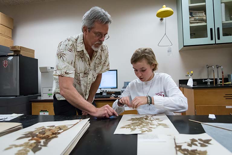 Director Eric Knox instructs Maggie Vincent on how to affix a label to a pressed plant specimen sheet.