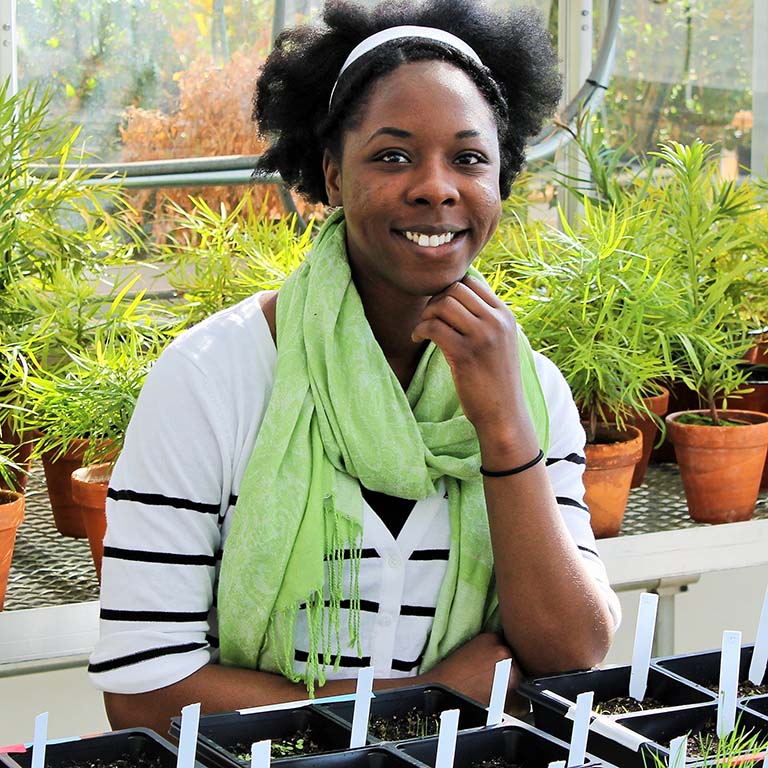 Lekeah Durden poses with her research plants in the Jordan Hall greenhouse.