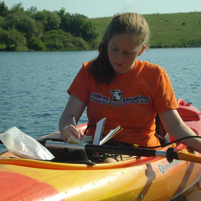 Marta Shocket in a kayak writes in her notebook while collecting samples from a lake in Greene-Sullivan State Forest in southern Indiana.