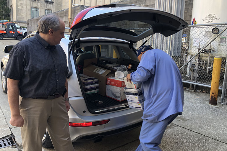 Health care workers loading donated personal protective equipment into vehicle.