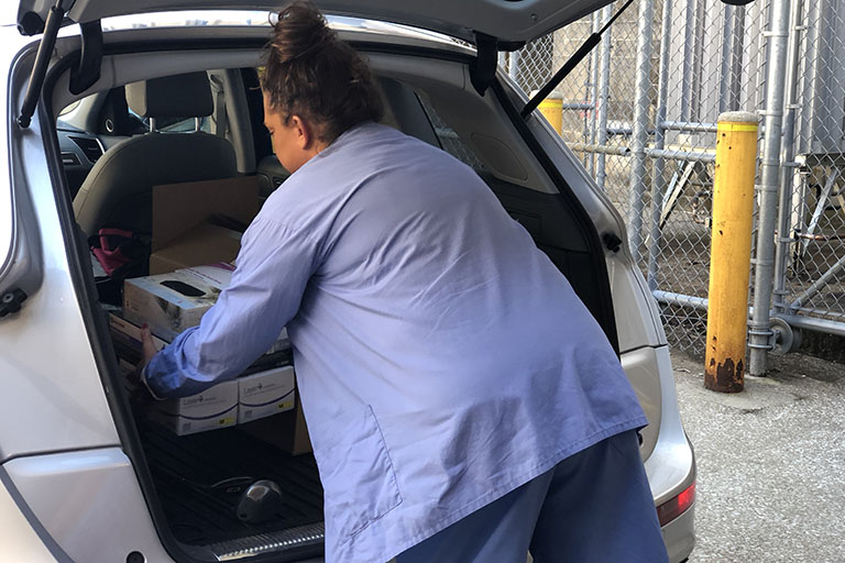 Health care worker loading donated personal protective equipment into vehicle.