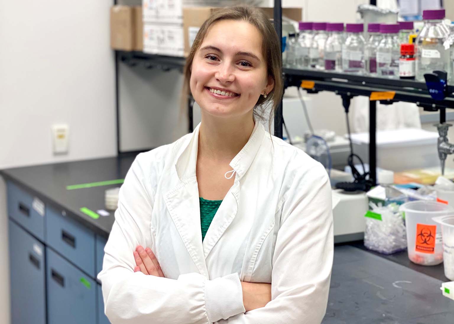 Emily Erdmann wears a white lab coat as she leans against a work bench in the lab.