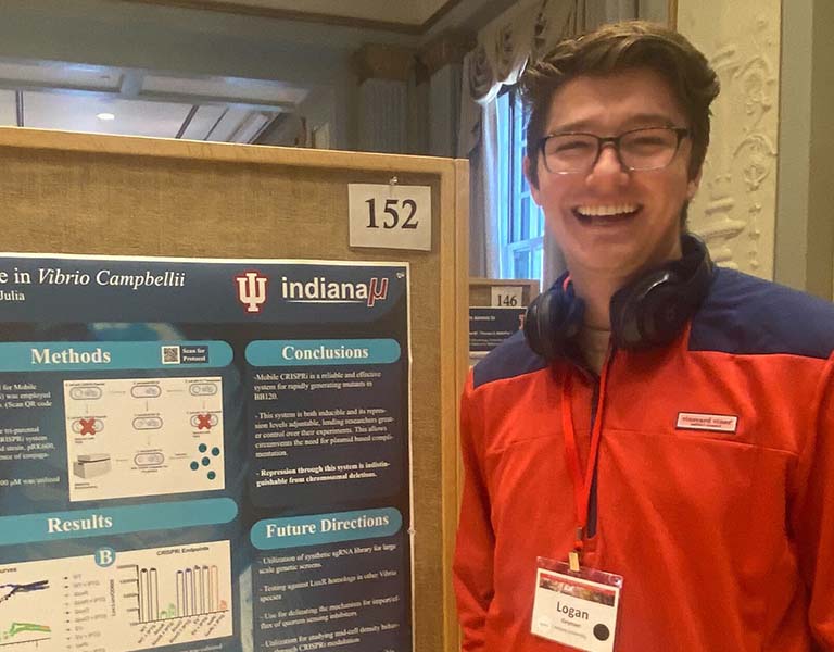 Logan Geyman poses with his poster presentation at the 2022 Midwest Microbial Pathogenesis Conference.